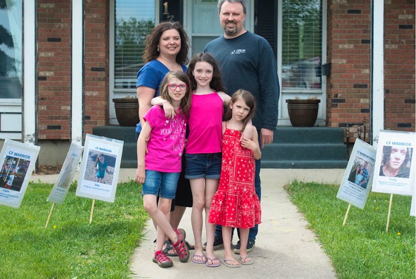 Twyla and Chris McDougall stand in their front yard with their three daughters (from left) Soleil, Emmanuella and Allegra McDougall in Regina on May 27, 2020. They are surrounded by lawn signs bearing the images of "CF warriors." Emmanuella was born with cystic fibrosis and, as a result, the family has long been accustomed to wearing masks and avoiding people who are sick.