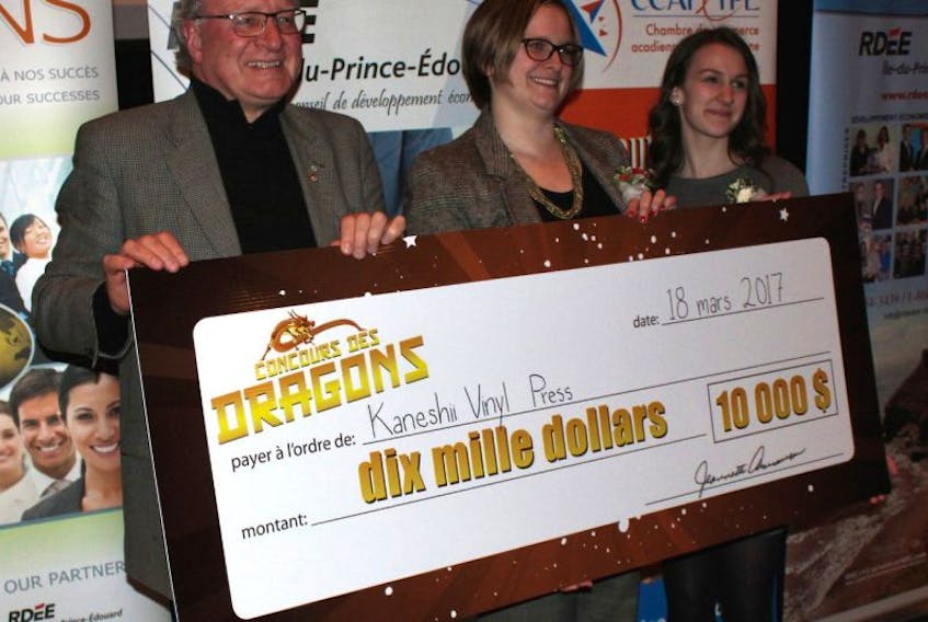 Premier Wade MacLauchlan helps Nicole Allain, right, coordinator of the 2017 Dragons' Contest, present the huge $10,000 cheque to champion Ghislaine Cormier of Charlottetown, who is setting up Kaneshii Vinyl Press.