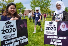 Caroline Trinh, left, and Fatima Al-Qaysi, right, present their signs during a surprise graduation event recently at Colonel Gray High School in Charlottetown.