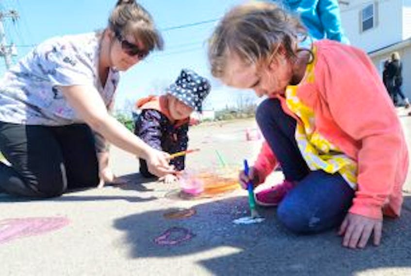 ['Ida Mitchell, early childhood educator, Maelle Gillan and Autumn MacLeod paint chalk hearts on the pavement at the Milestone Early Years and Child Care Centre.']