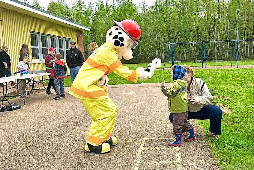 Sparky, the mascot of the Wentworth Volunteer Fire Department, gets a high five from Caleb Seymour with his mother Sonya Seymour kneeling beside him during community fun day in Wentworth.