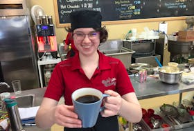 Haley Bishop of Kate's Bakery in New Minas holds a ceramic mug of coffee Tuesday. Like other small shops, Kate's is still using the mugs and filling reusable mugs for customers.