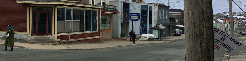 In April, a woman with a mask walks along Freshwater Road in St. John's while on the opposite side of the street, a "Six feet part or six feet under" sign flaps on a utility pole. The metro scene this summer is vastly different as COVID-19 restrictions eased and cases plumetted to zero most days. BARB SWEET/THE TELEGRAM