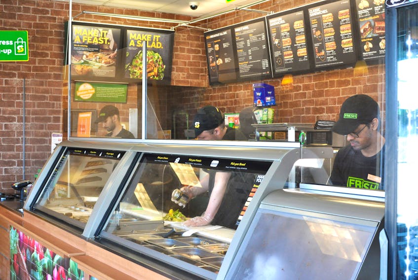 Workers at the Subway on Union Street in Corner Brook, from left, Kaleem Kurmoo, Daryl Eames and Jay Vispute work behind the plexiglass installed at the restaurant. Subway is now offering delivery though Island Eats. – Diane Crocker