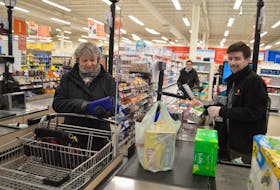 Fiona Grant, left, of Beaver Cove, waits as her grocery items are rung in by Breton MacLeod, a cashier at the Atlantic Superstore in Sydney River, Tuesday. The huge pieces of plexiglass are one of many measures Loblaws has implemented in their stores to create a social distancing safe barrier for employees and customers during the COVID-19 crisis. Sharon Montgomery-Dupe/Cape Breton Post