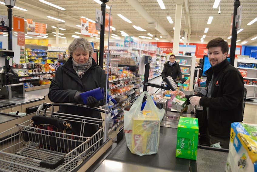 Fiona Grant, left, of Beaver Cove, waits as her grocery items are rung in by Breton MacLeod, a cashier at the Atlantic Superstore in Sydney River, Tuesday. The huge pieces of plexiglass are one of many measures Loblaws has implemented in their stores to create a social distancing safe barrier for employees and customers during the COVID-19 crisis. Sharon Montgomery-Dupe/Cape Breton Post