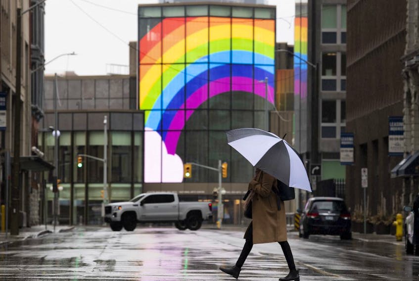 A large rainbow is shown on the National Arts Centre as a woman walks across a quiet street in downtown Ottawa, Tuesday, April 21, 2020 in Ottawa. 