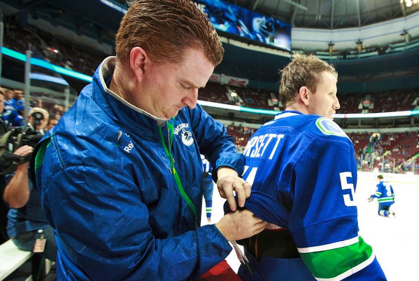 Vancouver Canucks assistant equipment manager Brian Hamilton adjusts Derek Dorsett's equipment before an NHL game.