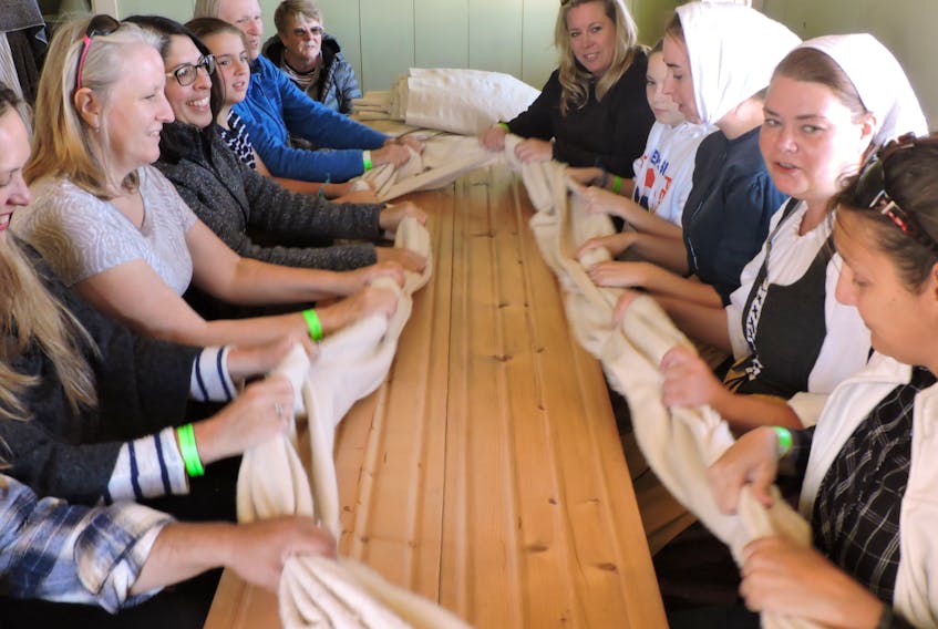 Iona's Highland Village Museum animator Stacey MacLean leads a group of visitors in a milling frolic, a traditional communal activity that involves gathering to process woolen fabric while singing traditional Gaelic songs.