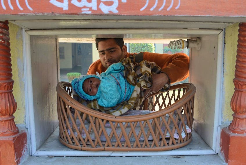 Indian Red Cross Society employee Ashwani Kumar poses with an abandoned baby girl, found at the pictured "pangpura" (cradle) drop off box at the entrance of the Red Cross House in Amritsar on January 21, 2013.