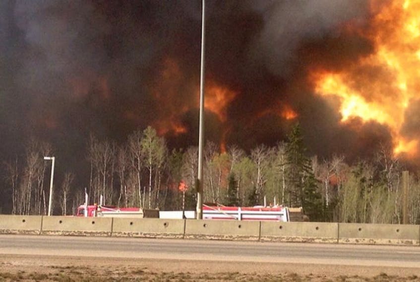 Trees burn near a road in Fort McMurray, Alberta on Tuesday May 3, 2016 in this image provide by radio station CAOS91.1. At least half of the city of Fort McMurray in northern Alberta was under an evacuation notice Tuesday as a wildfire whipped by winds engulfed homes and sent ash raining down on residents. T