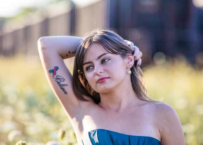 Briana Fletcher shows a ribbon tattoo on her arm, a symbol of infertility. Fletcher, at 16, was diagnosed with Mayer-Rokitansky-Küster-Hauser (MRKH) syndrome, a rare disorder characterized by the Müllerian duct's failure to develop, resulting in her being born without a womb. - Jan Wan Photography
