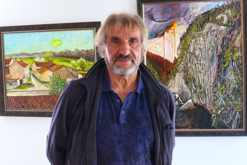 Jean Claude Roy stands between two of his new paintings at the Emma Butler Gallery in downtown St. John's. The painting on the left was painted while he strapped himself to the top of his stone farmhouse in La Clisse, France. The painting on the right was painted while sitting on the La Manche suspension bridge on the East Coast Trail. — Andrew Waterman/The Telegram