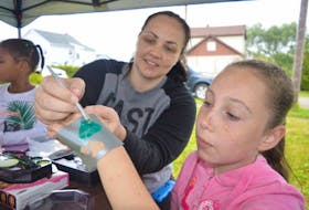 <p>Tiffany Turner, left, a volunteer with the Universal Negro Improvement Association, puts the finishing touches on a glitter tattoo for Lanaya Headley, 10, of Glace Bay, during Marcus Garvey Days celebrations, Thursday.&nbsp; Celebrations continue for all ages including a children’s barbecue and games Friday and a senior’s spa Saturday.</p>