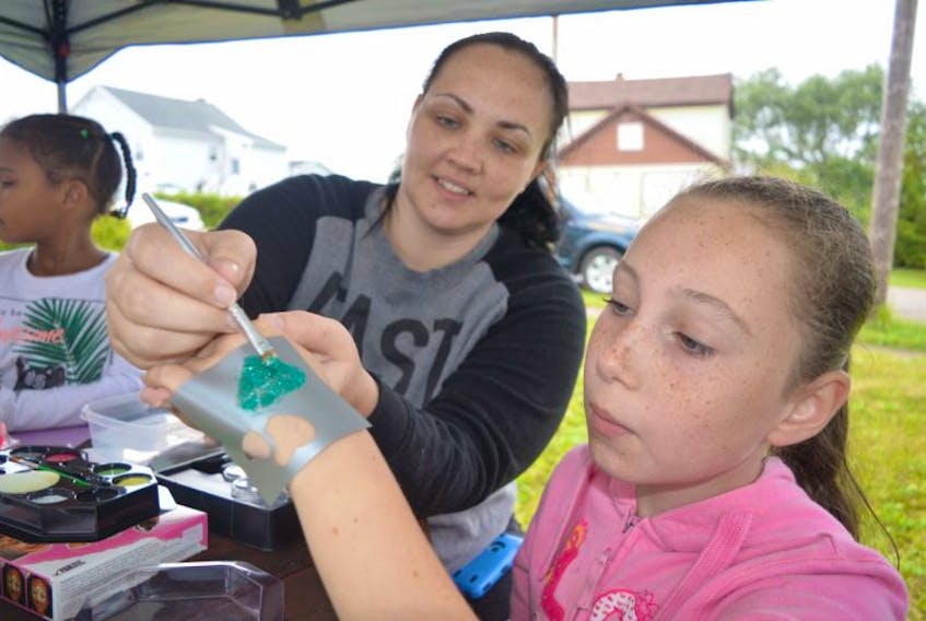 <p>Tiffany Turner, left, a volunteer with the Universal Negro Improvement Association, puts the finishing touches on a glitter tattoo for Lanaya Headley, 10, of Glace Bay, during Marcus Garvey Days celebrations, Thursday.&nbsp; Celebrations continue for all ages including a children’s barbecue and games Friday and a senior’s spa Saturday.</p>