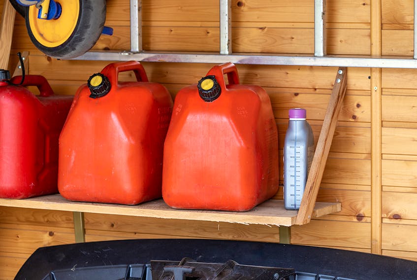 Garage corner with three red plastic fuel cans , staircase and snow plough for atv with wooden wall on background. Petrol gas containers reserves storage at vehicle home garage.