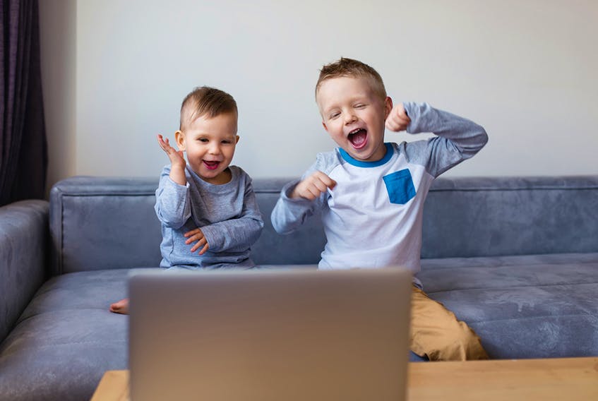 Two cute siblings using laptop while sitting on sofa