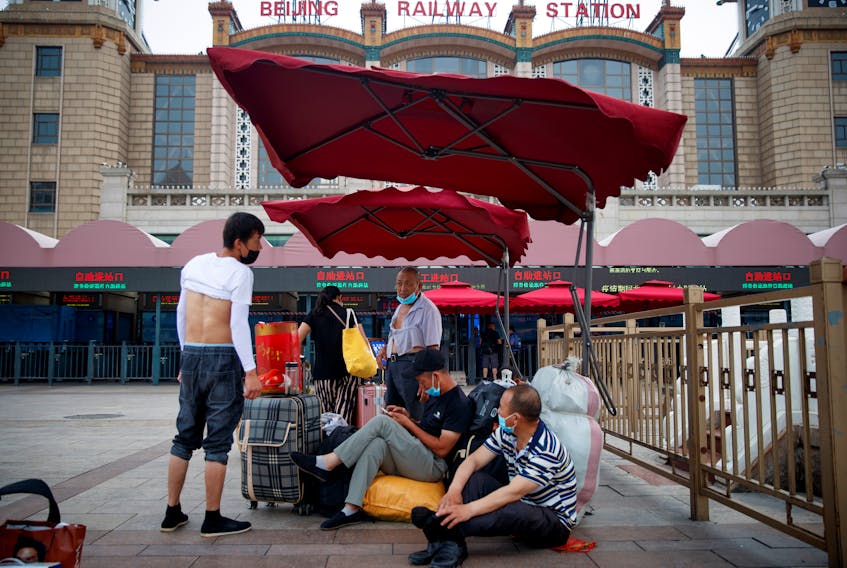 People sit on their luggage outside the Beijing Railway Station, after an outbreak of the coronavirus disease (COVID-19), in Beijing, China July 3, 2020. 