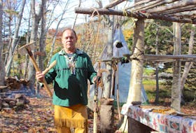 Charles Francis holds an axe and knife fashioned from moose antler, as well as an elaborately-carved walking stick that would have been a sign of wealth and status in traditional times.