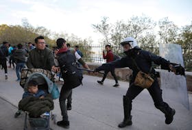 A riot police office hits a migrant with his baton as police tried to disperse a group of migrants outside the port of Mytilene, Greece, Wednesday. — Reuters

