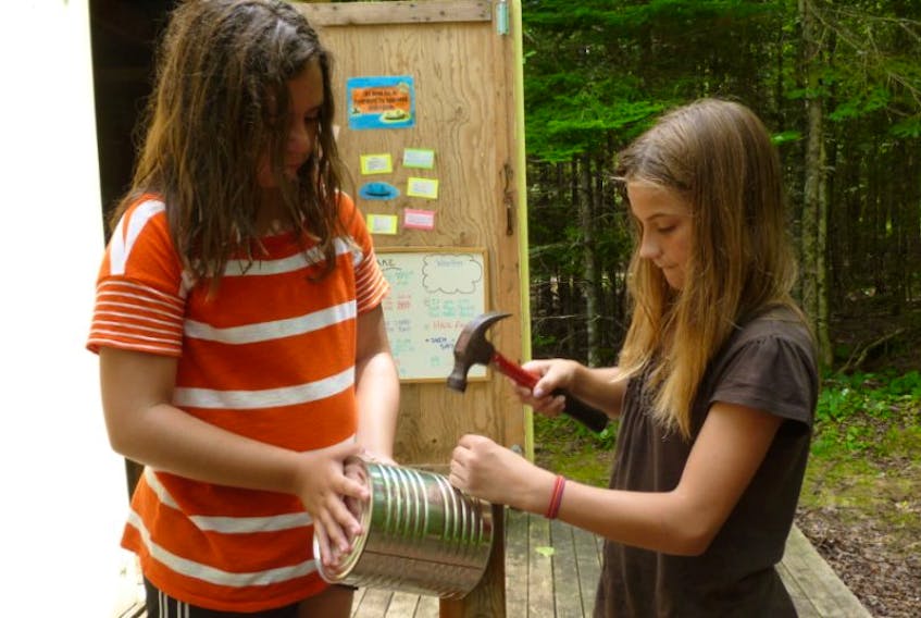 <p>Pathfinders Madison Leonard, left, and Lynn Llewellyn get set for lunch: punch a few holes for air circulation in a tin can, light a fire under it and cook a grilled cheese sandwich! Ta dah: a traditional tin can stove. - Submitted</p>