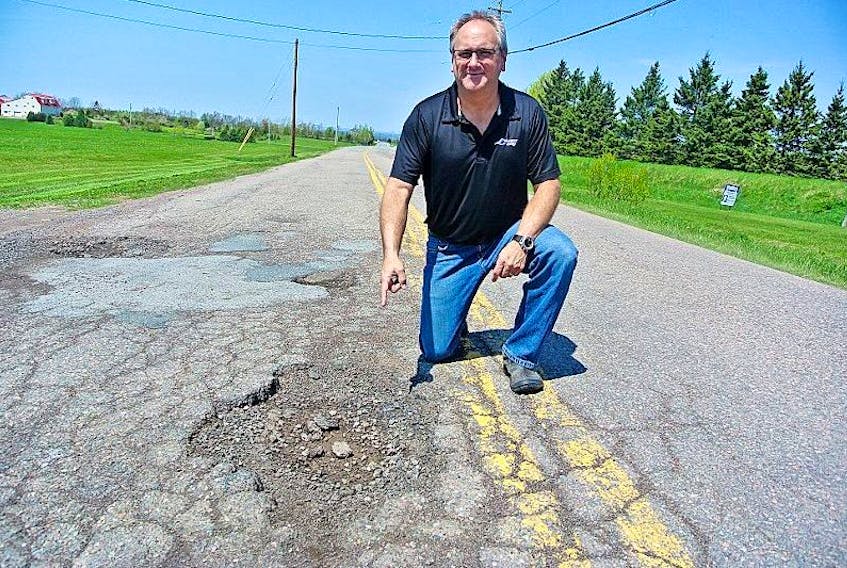 Greg Smith kneels next to Hastings Road pothole that recently claimed a tire on his vehicle. Smith and other residents have been lobbying the province to fix the road that has caused damage to residents’ vehicles. 
