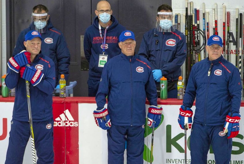  Montreal Canadiens head coach Claude Julien, centre, flanked by assistant coaches Kirk Muller, left, and Domenic Ducharme, right, keep an eye on practice as support staff wearing protective equipment look on as they hold their first team practice on July 13, 2020, in Brossard.