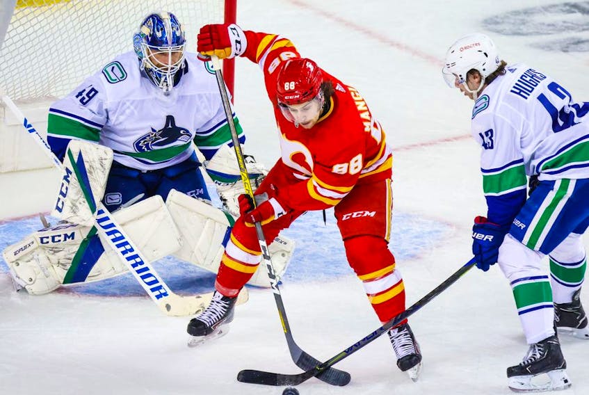 Calgary Flames forward Andrew Mangiapane and Vancouver Canucks defenceman Quinn Hughes battle for the puck in front of Vancouver goaltender Braden Holtby at the Scotiabank Saddledome in Calgary on Jan. 16, 2021.