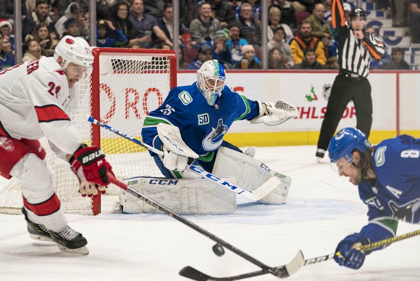 Vancouver Canucks  goalie  Jacob Markstrom (25)) looks on as Carolina Hurricanes forward  Nino Niederreiter (21) battles with Vancouver Canucks  defenceman Christopher Tanev (8) in the second period at Rogers Arena. 