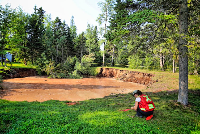 An official with Energy and Mines Nova Scotia takes a measurement near the giant sinkhole in the Lions Park in Oxford. Activity around the sinkhole has slowed for the third consecutive day, although it has undermined a small portion of the parking lot for the community centre.