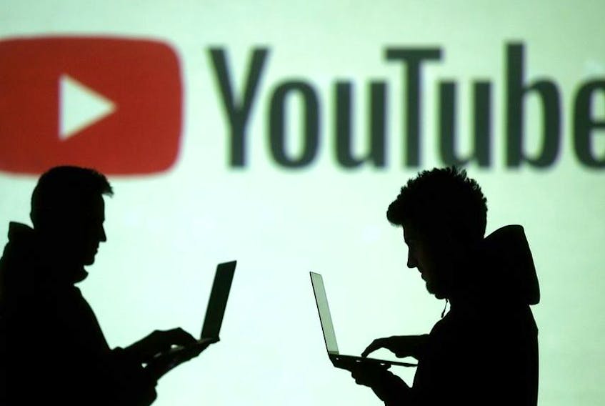Silhouettes of mobile device users are seen next to a screen projection of Youtube logo in this picture illustration taken March 28, 2018.  