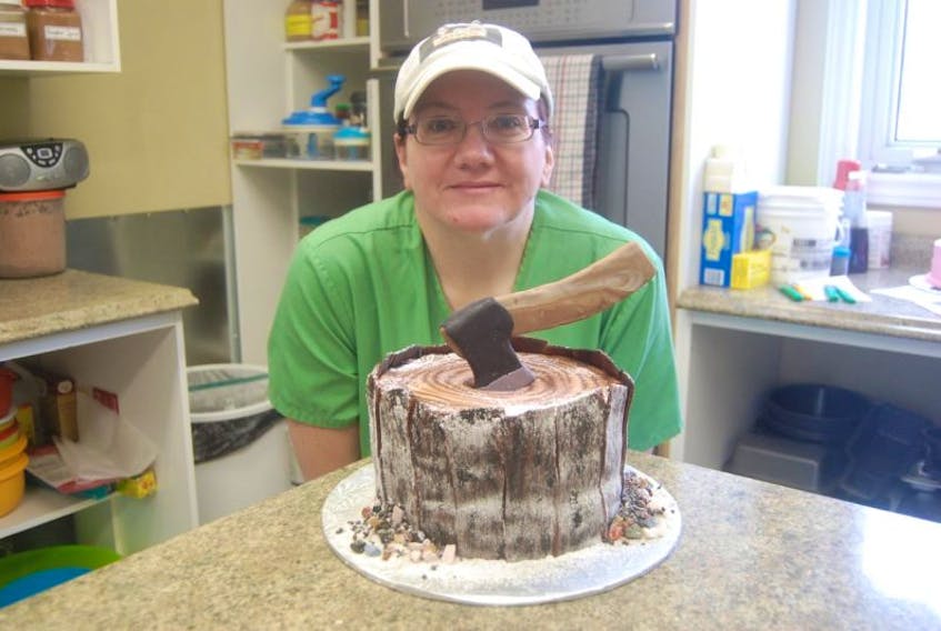 Jennifer Evans poses with a lumberjack cake she made, featuring an axe in a stump with all edible components.