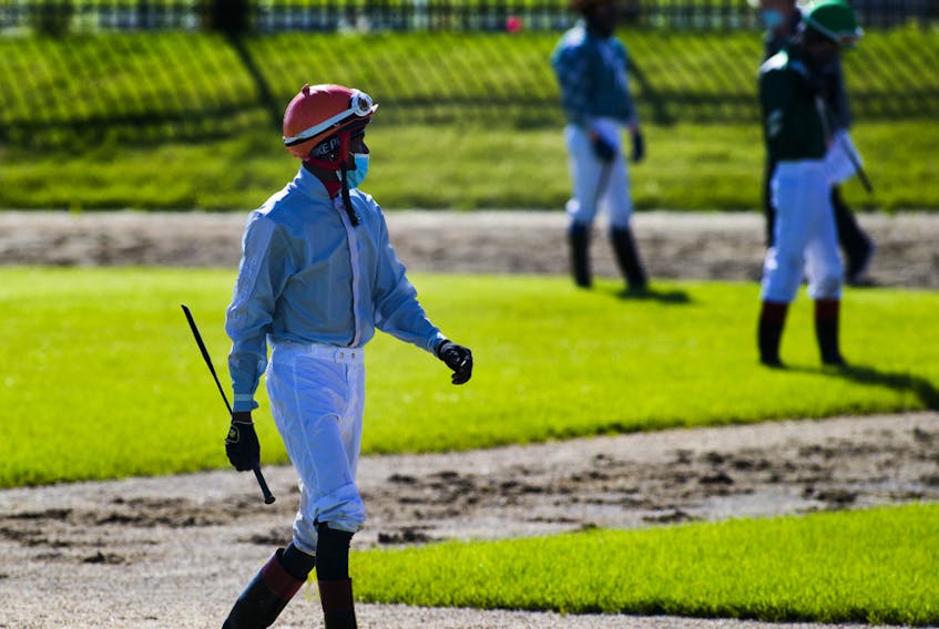 Jockeys enter the paddock wearing masks before the first race on opening day of the season for Century Mile Racetrack on Sunday, June 21, 2020. No fans were allowed in the stands, just jockeys, horses and trainers.