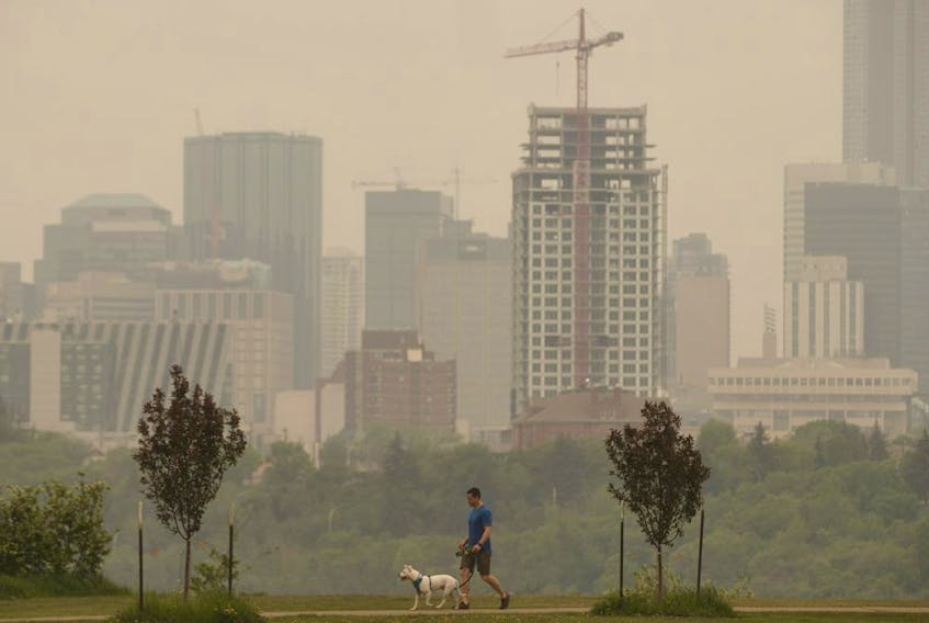A person walks their dog as smoke blankets the city from nearby wildfires, in Edmonton on Thursday, May 30, 2019.