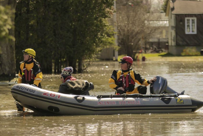 Firefighters move a man down a flooded street in Ste-Marthe-sur-le-Lac on Sunday April 28, 2019, the day after a dike was breached in the town.