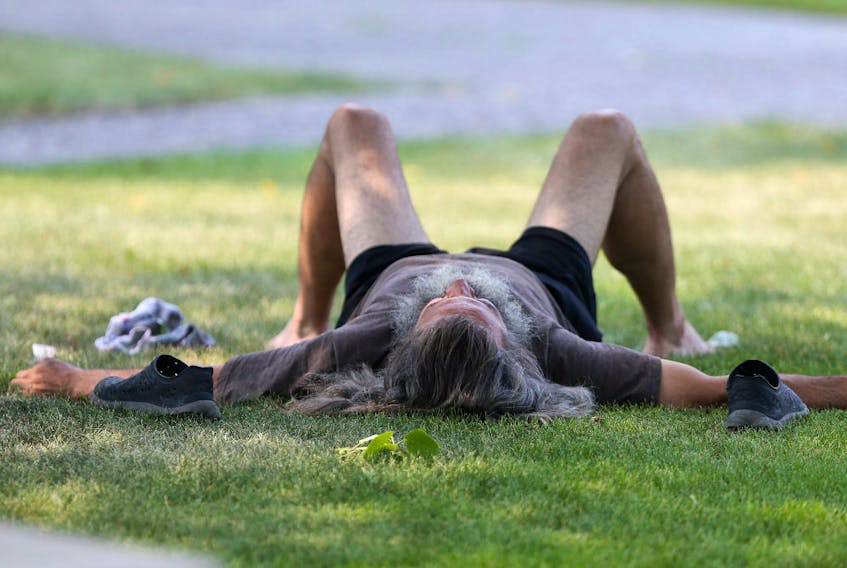 A man with long grey hair and a large beard relaxes in the shade in Memorial Park, during a heat wave in Winnipeg in August 2018.
