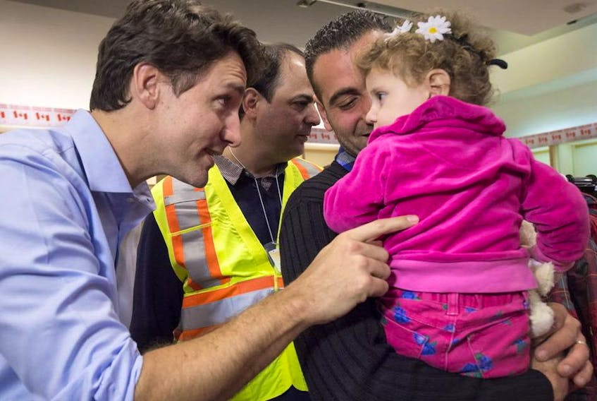 Prime Minister Justin Trudeau greets 16-month-old Madeleine Jamkossian, right, and her father Kevork Jamkossian, refugees fleeing the Syrian civil war, during their arrival at Pearson International airport, in Toronto on Dec. 11,  2015.