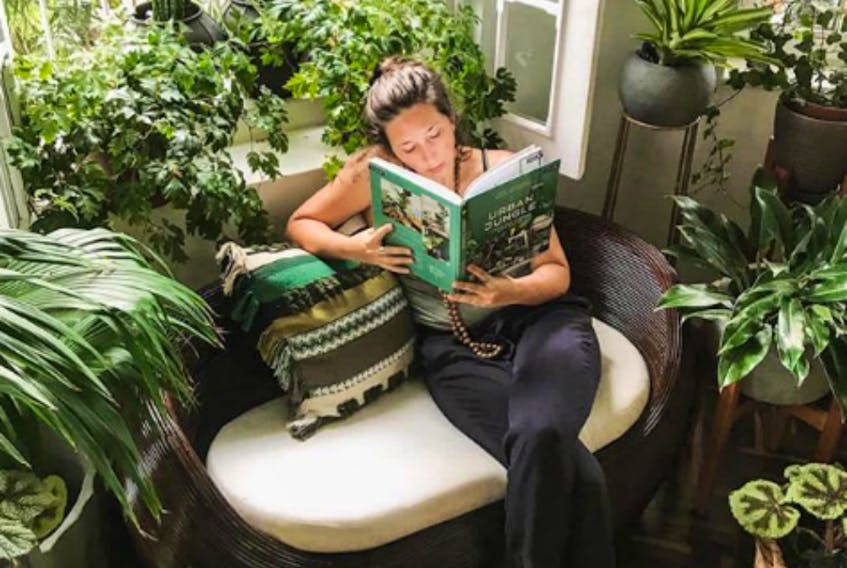 A woman reads amongst plants. 
