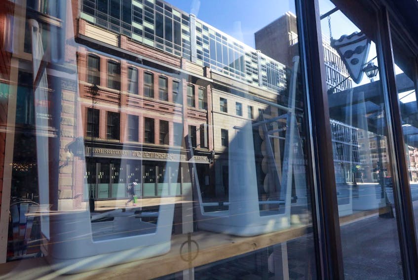 A pedestrian walks along the other side of Barrington Street in downtown Halifax on Wednesday, March 25, 2020, reflected in the window of a restaurant shuttered because of the COVID-19 outbreak.