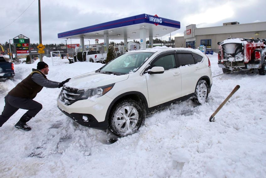 Good Samaritans push and use a chain attached to a truck to free an SUV stuck in the snow at an Irving station on Lacewood Drive in Halifax on Monday, Feb. 8, 2021.