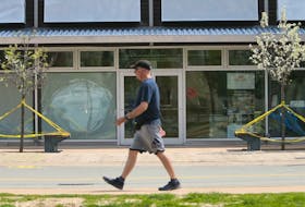 A man strolls past benches taped off to prevent sitting, outside the Halifax Seaport Farmers' Market, also closed, in Halifax, Wednesday, May 27, 2020.