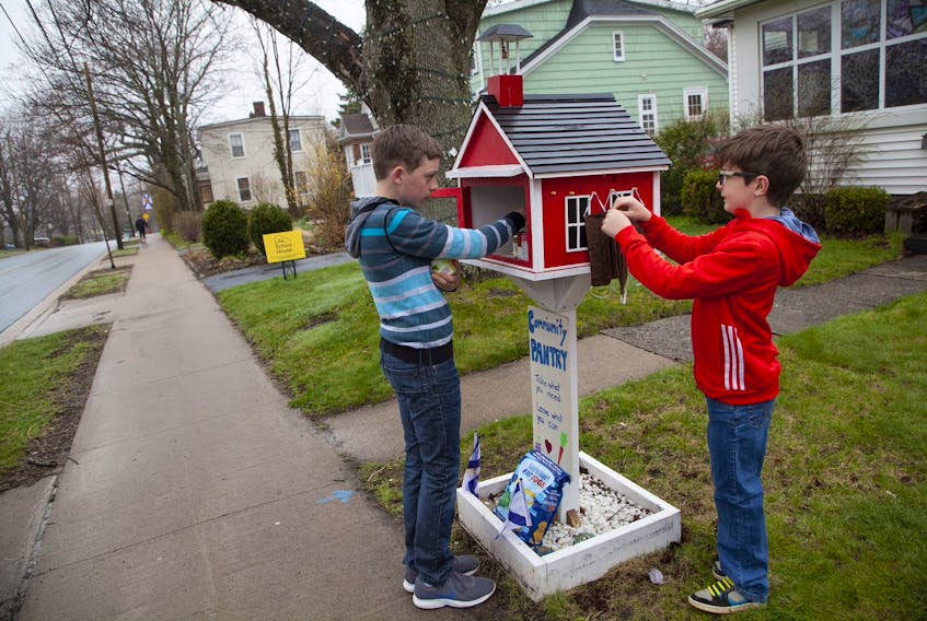 Rylan, 13, and Bren DeCoste, 8, put non-perishables and face masks into the School House pantry on the front lawn of their Dartmouth home Monday, May 4, 2020. Their mother Jennifer said that the food is going out quickly these days.