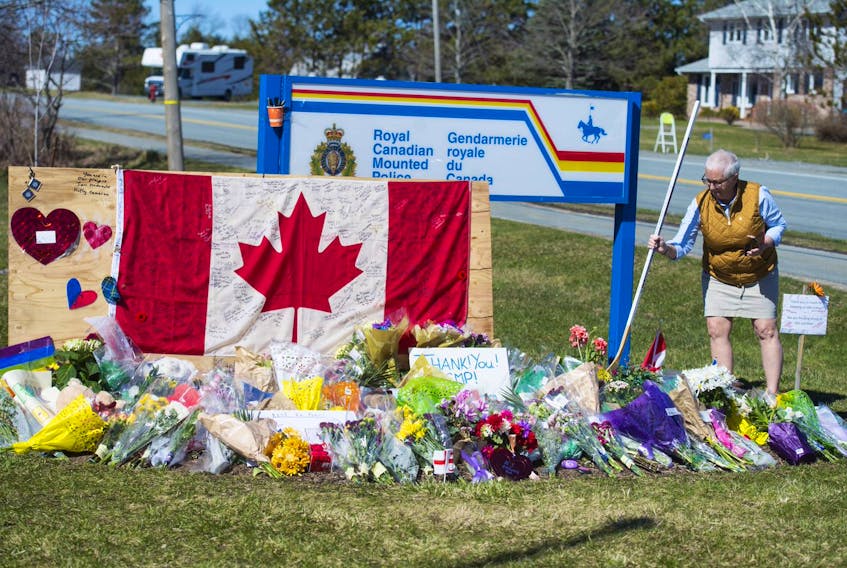 Trina Norman, president of the Windsor Hockey Heritage Society, places a hockey stick at a memorial to Const. Heidi Stevenson outside the Enfield RCMP detachment on Tuesday, April 21, 2020. The blade of the stick says: "With the deepest of gratitude and respect for your service, Cst. Heidi Stevenson - End of watch."