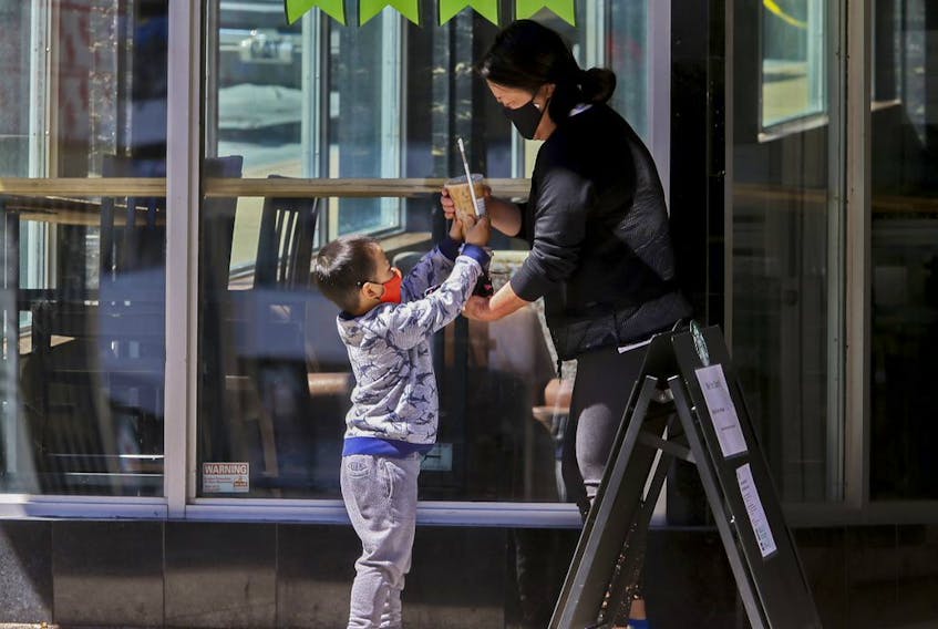 A youngster reaches up for his chocolate milk treat from his mother,  as they leave a coffee shop on Barrington Street in Halifax Wednesday, May 20, 2020.