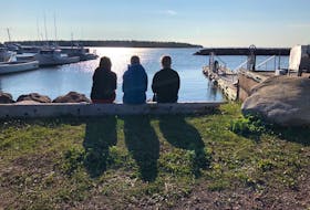 Three members of the community wait on shore as the last teen, Alex Hutchinson, is brought home Thursday morning in Northport, P.E.I.