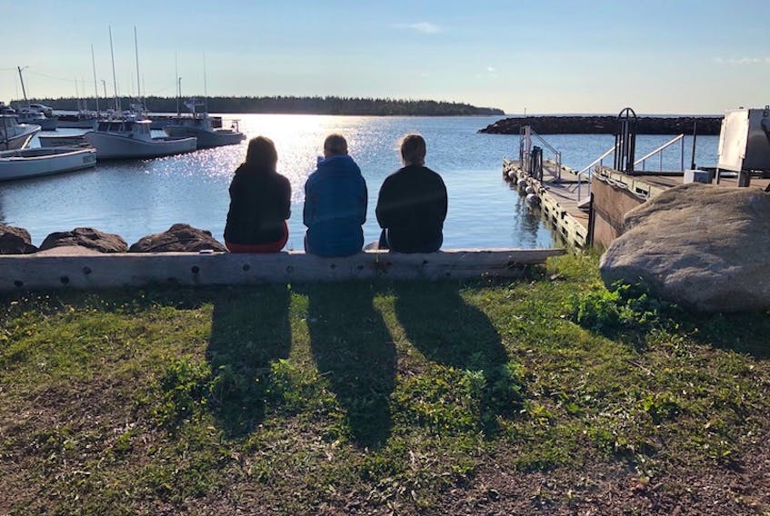 Three members of the community wait on shore as the last teen, Alex Hutchinson, is brought home Thursday morning in Northport, P.E.I.