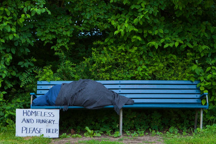 Homeless person on a park bench asks for help. STOCK IMAGE