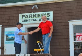 Craig Parker and Dick Killam shake hands after removing the paper from the Parker’s General Store sign.