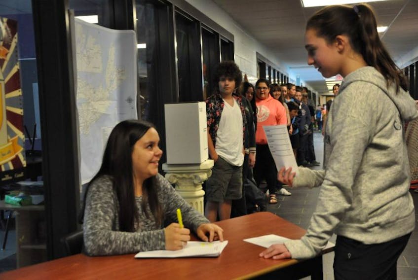 Ella Comeau, left, greets a classmate while pretending to be a returning officer for a mock election exercise offered through the Student Vote Nova Scotia program.