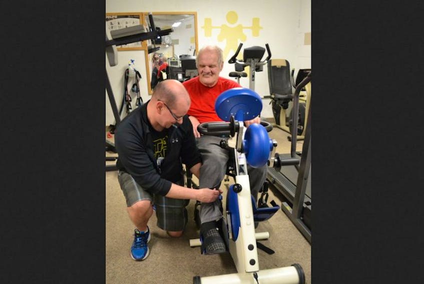 Darcy Huntley assists Kings Regional Rehabilitation Centre client Harry O’Neil properly position on the adaptable motorized exercise bike recently donated to the KRRC Fitness Room by the Apple Tree Foundation.